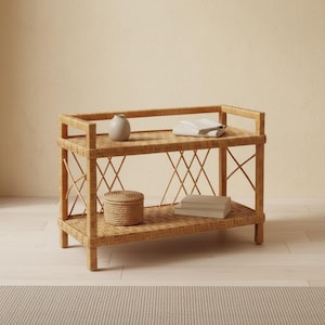 May include: A two-tiered light brown woven rattan console table with a rectangular frame and crisscross side supports. The top shelf holds a small beige vase and folded white cloth, while the bottom shelf holds a woven lidded box and books.