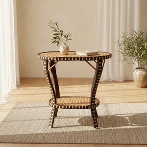 May include: A round side table featuring a woven light brown surface and a lower shelf, supported by four curved legs with dark brown and white checkered accents. A small white vase with green leaves and a closed book sit on the tabletop.