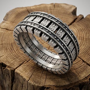 May include: A silver ring featuring a detailed railroad track design with two parallel rails and textured cross ties. The band has a smooth interior surface with a 925 hallmark stamp visible. The metal has an oxidized finish to highlight the intricate details of the railway motif throughout the entire circumference of the band.