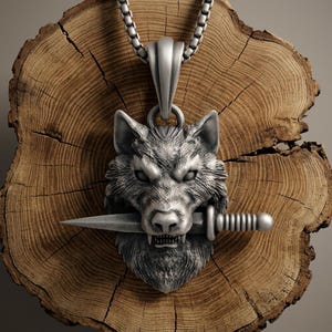 May include: A silver-toned pendant featuring a detailed wolf head with a dagger held horizontally in its mouth. The pendant is suspended from a thick silver-toned chain link necklace, showcasing intricate fur textures and sharp canine teeth.