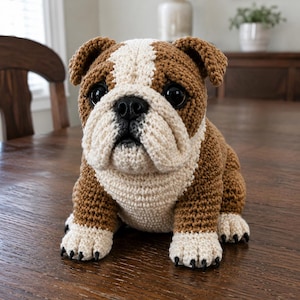 Può includere: Una statuetta di bulldog all'uncinetto realizzata con filato marrone e crema. Il cane presenta una striscia bianca sulla fronte, muso e petto color crema e orecchie marrone scuro. Include occhi in plastica neri e un naso nero.