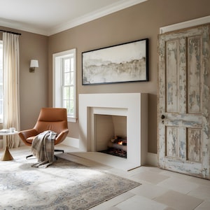 May include: A room featuring a tan leather swivel chair with a plaid throw blanket, a white fireplace with a fire inside, a rectangular abstract landscape painting in a black frame, and a weathered wooden door with peeling paint on a stone floor.