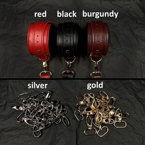 May include: Three leather cuffs in red, black, and burgundy, each featuring a gold-tone metal stud and a lobster clasp attachment. Below are two piles of metal hardware: one pile of silver-tone lobster clasps and one pile of gold-tone lobster clasps.