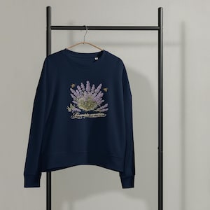 Könnte beinhalten: Ein dunkelblaues Langarm-Sweatshirt mit einer zentralen Grafik aus violetten Lavendelzweigen und zwei kleinen Bienen. Unter dem Lavendel ist der Text Lavandula angustifolia in einer dekorativen, hellen Schreibschrift aufgedruckt.