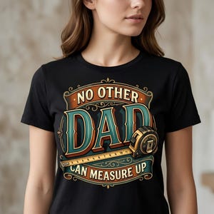May include: A black t-shirt featuring a graphic design with the text NO OTHER DAD CAN MEASURE UP. The design includes a teal and orange vintage-style frame and a yellow measuring tape with visible metric markings across the centre of the text.