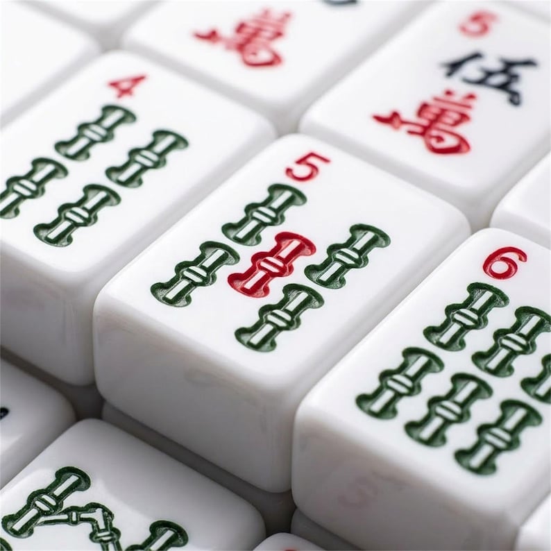 May include: Close-up of white Mahjong tiles. The tiles feature green bamboo symbols and red or black numbers and characters. The tiles are arranged closely together, creating a pattern.