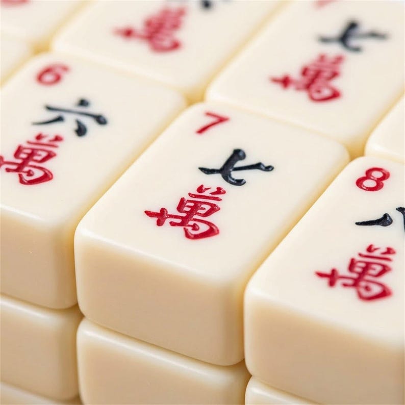 May include: Close-up of ivory-coloured Mahjong tiles. The tiles have black and red symbols and numbers. The number 7 tile is in focus, with the number and symbol clearly visible. The tiles are stacked together.