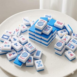 May include: A collection of white and blue Mahjong tiles. The tiles have various symbols, numbers, and Chinese characters in red and blue. Some tiles are stacked, while others are scattered on a white surface.