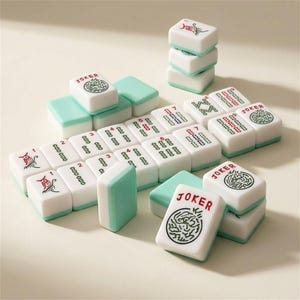 May include: A set of white and teal Mahjong tiles. The tiles have red and green symbols and numbers. Some tiles are stacked, and others are arranged in rows. The word "JOKER" is printed on some tiles.