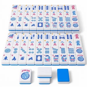 May include: A complete Mahjong set with white tiles featuring blue and red symbols and characters. The set includes tiles with numbers, suits, and special symbols, along with white and blue accessories. The tiles are neatly arranged.
