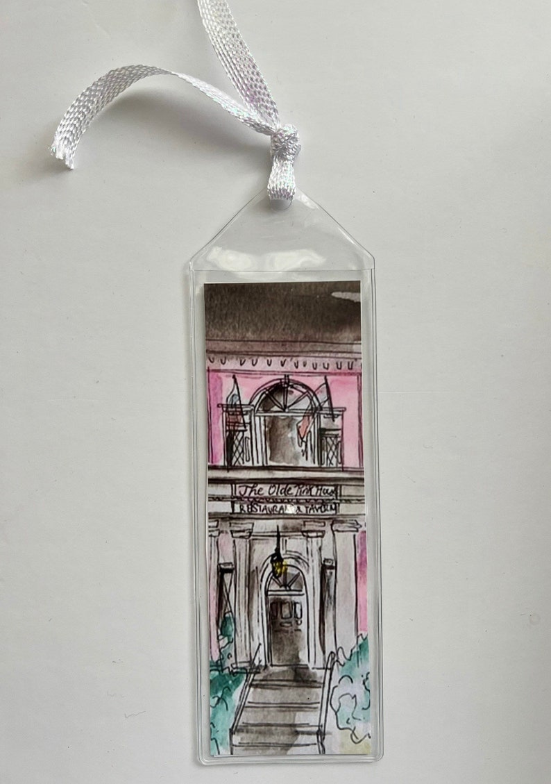 May include: A clear plastic bookmark with a watercolor illustration of a pink building with a sign that reads "The Olde Brick House Restaurant & Tavern".