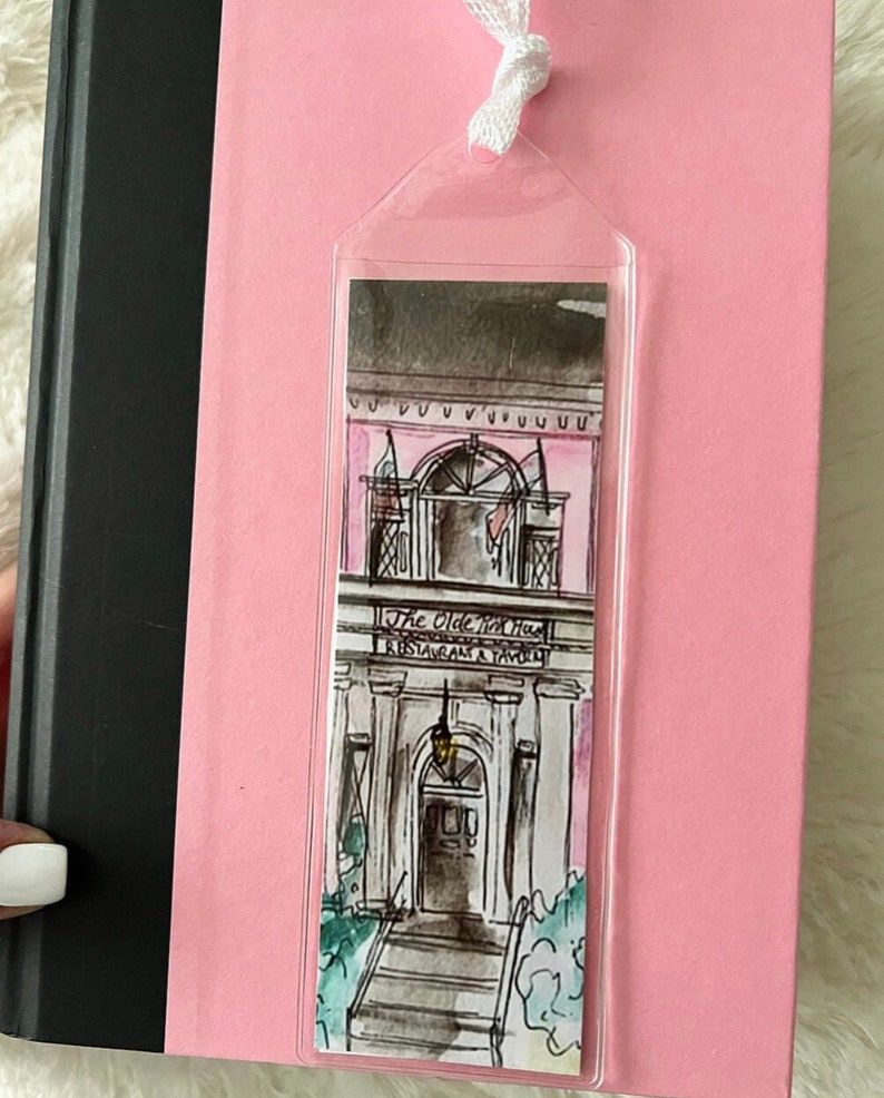 May include: A pink and white illustrated bookmark featuring a building with the text "The Olde Pink House Restaurant & Tavern".