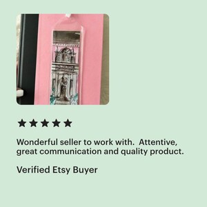 May include: A clear bookmark with a black and white illustration of a pink building with a white door and a balcony. The bookmark is hanging from a string.