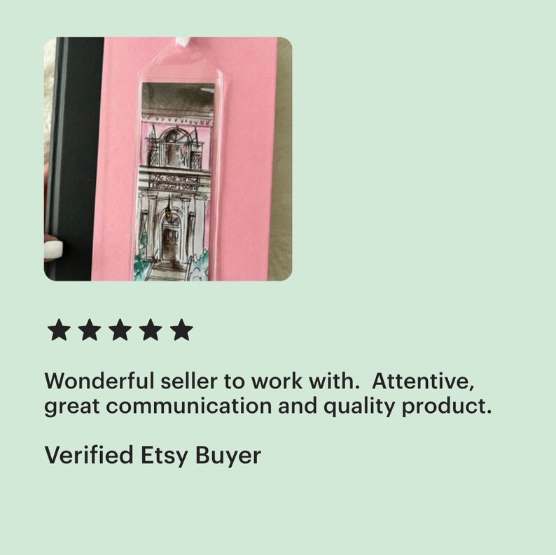 May include: A clear bookmark with a black and white illustration of a pink building with a white door and a balcony. The bookmark is hanging from a string.