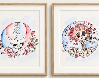 May include: Two framed watercolor prints in light wood frames. The left print features a skull with a blue and red lightning bolt design surrounded by pink roses. The right print shows a skeleton wearing a crown of red roses against a blue circle.