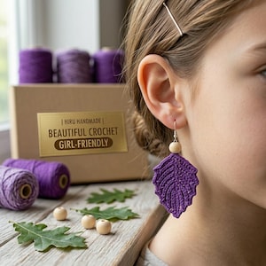 May include: A close-up of a purple crochet leaf earring with a wooden bead and silver hook. The earring is part of a set with a box that says "HIRU HANDMADE | BEAUTIFUL CROCHET GIRL-FRIENDLY".