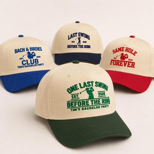 May include: Four baseball caps with text and golf-themed graphics. The caps are cream-colored with colored brims in blue, navy, red, and green. Text includes "Bach & Birdies Club," "Last Swing Before The Ring," "One Last Swing Before The Ring," and "Same Hole Forever."