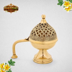 May include: A gold-colored incense burner with a decorative, pierced lid and a curved handle. The burner has a round base and a detailed pattern around the top. The design is ornate and traditional, suitable for home decor or spiritual practices.