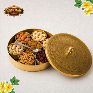 Op de afbeelding: Een ronde goudkleurige metalen bak met zes interne vakken gevuld met diverse noten en gedroogd fruit, waaronder amandelen, cashewnoten, rozijnen, pistachenoten, walnoten en veenbessen, vergezeld van een kleine zilverkleurige lepel.