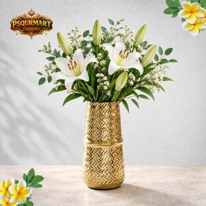 May include: A gold-colored vase with a textured chevron pattern holds a bouquet of white lilies, green foliage, and small white flowers. The vase features a horizontal band dividing the pattern. The logo PSQURMART ONLINE SHOP is visible.