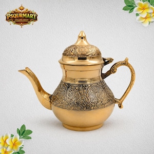 May include: A polished brass teapot featuring an intricate engraved pattern of stylized peacocks and floral motifs. The vessel includes a curved spout, a decorative lid with a pointed finial, and a sturdy handle. The logo PSQURMART is visible.