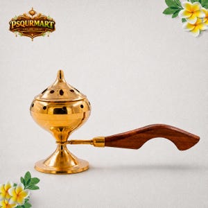 May include: A polished gold-toned metal incense burner featuring a rounded, perforated lid and a flared base. The burner is attached to a curved, dark brown wooden handle, providing a functional grip for this decorative vessel.