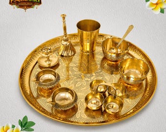 Op de afbeelding: Een gouden puja thali set van messing met diverse items, waaronder kommen, een bel, een beker en olielampen. De thali heeft een reliëf bloemenontwerp. De tekst "PSQURMART ONLINE SHOP" is inbegrepen.