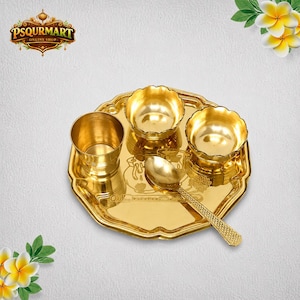 May include: A golden-colored, ornate serving set. The set includes a tray, two scalloped bowls, a small cup, and a spoon. The tray and spoon feature detailed patterns. The set is likely used for religious or ceremonial purposes.