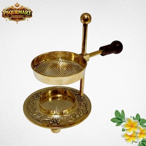 May include: A gold-coloured incense burner with a round base and a perforated bowl. The burner has a handle with a dark brown wooden grip. The base features an embossed floral design. The top of the burner has a small ball.