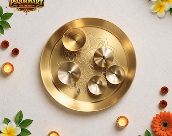 Op de afbeelding: Een gouden metalen puja thali set met een decoratief bloemmotief. De set bevat een grote ronde dienblad, een kleine kom en vijf kleine kaarshouders. De afbeelding is versierd met bloemen en kaarsen.