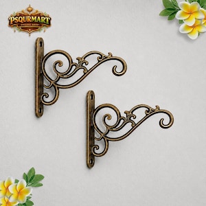 May include: Two antique brass-colored metal wall brackets featuring ornate scrollwork designs. Each bracket has a vertical mounting plate with two circular screw holes and a curved arm extending outward to support hanging items.