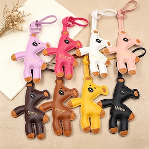Puede incluir: Colección de llaveros de cuero coloridos con forma de animales estilizados. Cada llavero presenta un color diferente, incluyendo rosa, blanco, amarillo y negro, con detalles marrones contrastantes. Los llaveros tienen un lazo para sujetar y un nombre.