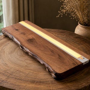 May include: A rectangular wooden board with a natural live edge on one side, featuring a long, integrated, rectangular LED light strip embedded flush into the surface. The light strip emits a soft, warm glow and includes a small circular sensor.