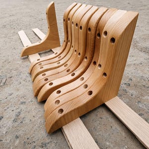 May include: A set of six curved light brown wooden shelf brackets arranged in a row. Each bracket features a smooth, polished finish with a series of pre-drilled circular holes along the side and top edges for mounting purposes.