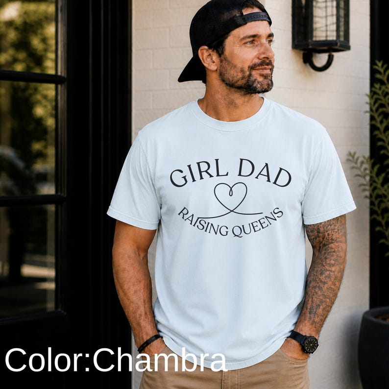 May include: A light blue t-shirt with the text "GIRL DAD RAISING QUEENS" in black. The shirt has short sleeves and a crew neck. The color is Chambra.