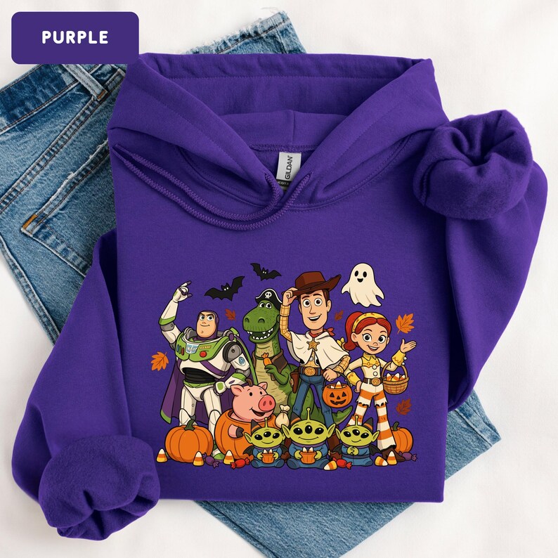 Puede incluir: Una sudadera con capucha morada que presenta un estampado gr&aacute;fico de personajes de Toy Story vestidos con disfraces de Halloween, incluyendo a Buzz Lightyear, Rex, Woody, Jessie, Hamm y tres alien&iacute;genas, rodeados de calabazas, murci&eacute;lagos y un fantasma.