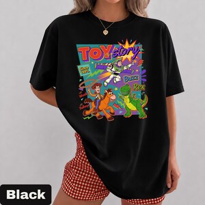 May include: Black t-shirt featuring a colorful graphic of Toy Story characters, including Woody, Buzz Lightyear, and Rex. The design includes the text "TOY Story" and "Since 1995." The shirt is a classic crew neck style.