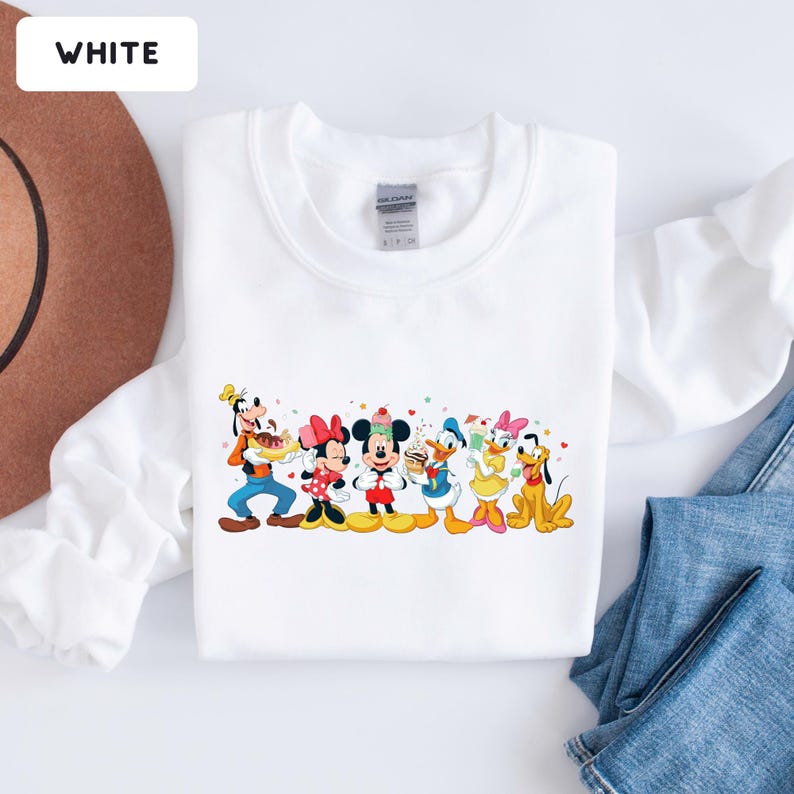 May include: A white crewneck sweatshirt featuring a colourful graphic print of Disney characters including Goofy, Minnie Mouse, Mickey Mouse, Donald Duck, Daisy Duck, and Pluto. The characters are depicted holding various treats and snacks.