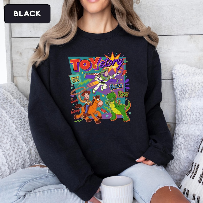 May include: Black sweatshirt featuring a colorful graphic from the movie "Toy Story." The design includes Woody, Buzz Lightyear, and Rex, with the text "Toy Story" and "Since 1995."