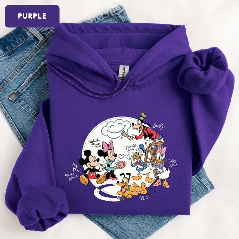 May include: A purple hooded sweatshirt featuring a graphic of Disney characters Mickey Mouse, Minnie Mouse, Donald Duck, Daisy Duck, Goofy, and Pluto. The sweatshirt has a drawstring hood and a kangaroo pocket.