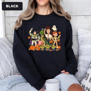 Puede incluir: Una sudadera negra de manga larga con un estampado gr&aacute;fico de personajes de Toy Story disfrazados para Halloween. El dise&ntilde;o incluye a Buzz Lightyear, Rex, Woody, Jessie, Hamm y tres alien&iacute;genas rodeados de calabazas, dulces y un fantasma.