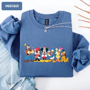 May include: An indigo crewneck sweatshirt featuring a graphic print of Disney characters including Goofy, Minnie Mouse, Mickey Mouse, Donald Duck, Daisy Duck, and Pluto. The characters are holding various treats. The text INDIGO is in the corner.