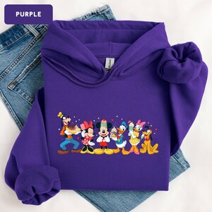 May include: A purple hooded sweatshirt featuring a graphic print of Disney characters including Goofy, Minnie Mouse, Mickey Mouse, Donald Duck, Daisy Duck, and Pluto, each holding various ice cream treats, with small colourful stars and hearts.