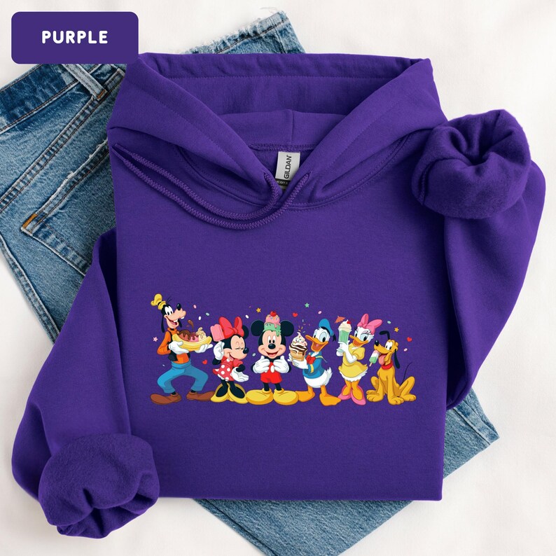 May include: A purple hooded sweatshirt featuring a graphic print of Disney characters including Goofy, Minnie Mouse, Mickey Mouse, Donald Duck, Daisy Duck, and Pluto, each holding various ice cream treats, with small colourful stars and hearts.