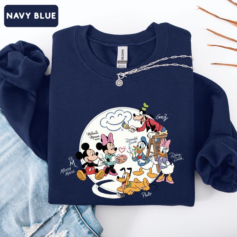 May include: Navy blue sweatshirt featuring a graphic of Mickey Mouse, Minnie Mouse, Donald Duck, Daisy Duck, Goofy, and Pluto. The characters are arranged around a cloud with the text "Mickey Mouse" and "Navy Blue". A silver necklace is draped on the sweatshirt.