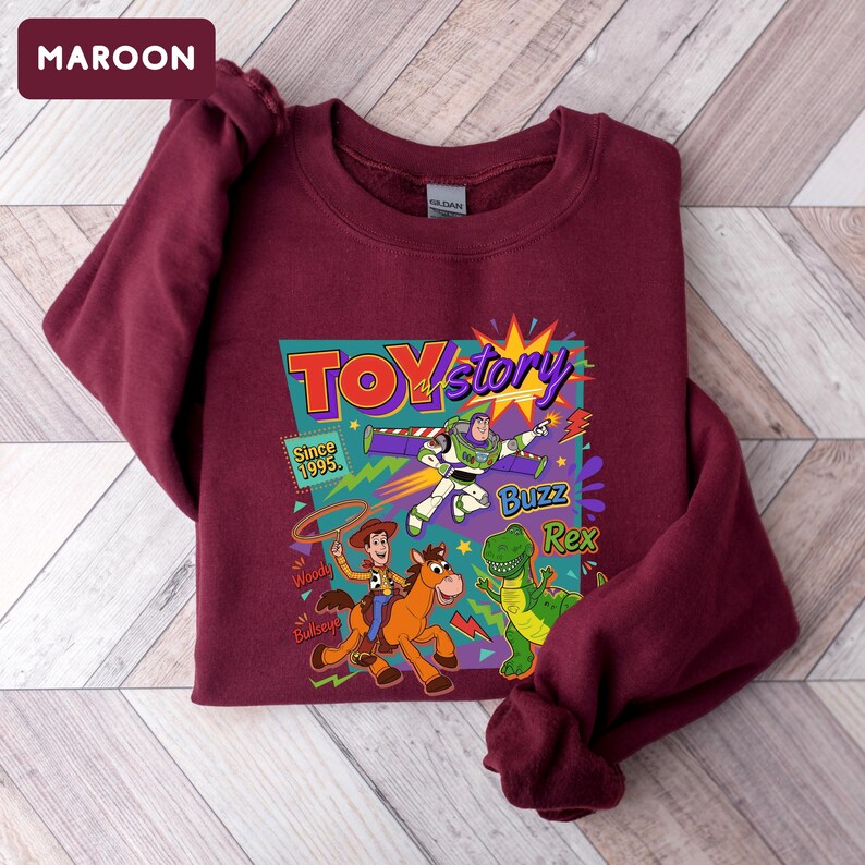 May include: Maroon sweatshirt featuring a colorful graphic from the movie Toy Story. The graphic includes the words "Toy Story" and the characters Buzz Lightyear, Woody, Bullseye, and Rex. The text "Since 1995" is also included.