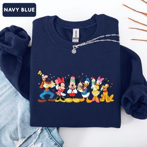 May include: A navy blue crewneck sweatshirt featuring a graphic print of Goofy, Minnie Mouse, Mickey Mouse, Donald Duck, Daisy Duck, and Pluto holding various ice cream treats. The text NAVY BLUE appears in a small box in the top left corner.