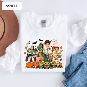 Puede incluir: Una sudadera blanca de manga larga con un gr&aacute;fico colorido de personajes de Toy Story disfrazados de Halloween, incluyendo a Buzz Lightyear, Woody, Jessie, Rex, Hamm y tres alien&iacute;genas, rodeados de calabazas, murci&eacute;lagos y hojas de oto&ntilde;o.