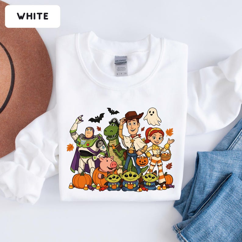 Puede incluir: Una sudadera blanca de manga larga con un gr&aacute;fico colorido de personajes de Toy Story disfrazados de Halloween, incluyendo a Buzz Lightyear, Woody, Jessie, Rex, Hamm y tres alien&iacute;genas, rodeados de calabazas, murci&eacute;lagos y hojas de oto&ntilde;o.