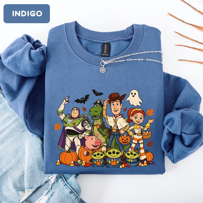 Puede incluir: Una sudadera de cuello redondo color &iacute;ndigo con un estampado gr&aacute;fico de personajes de Toy Story disfrazados para Halloween, incluyendo a Buzz Lightyear, Rex, Woody, Jessie, Hamm y tres alien&iacute;genas, rodeados de calabazas, murci&eacute;lagos, un fantasma y hojas de oto&ntilde;o.